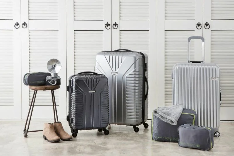 2 chiếc vali nhựa màu bạc và 1 chiếc màu đen đặt cạnh những túi đồ và máy ảnh trong phòng